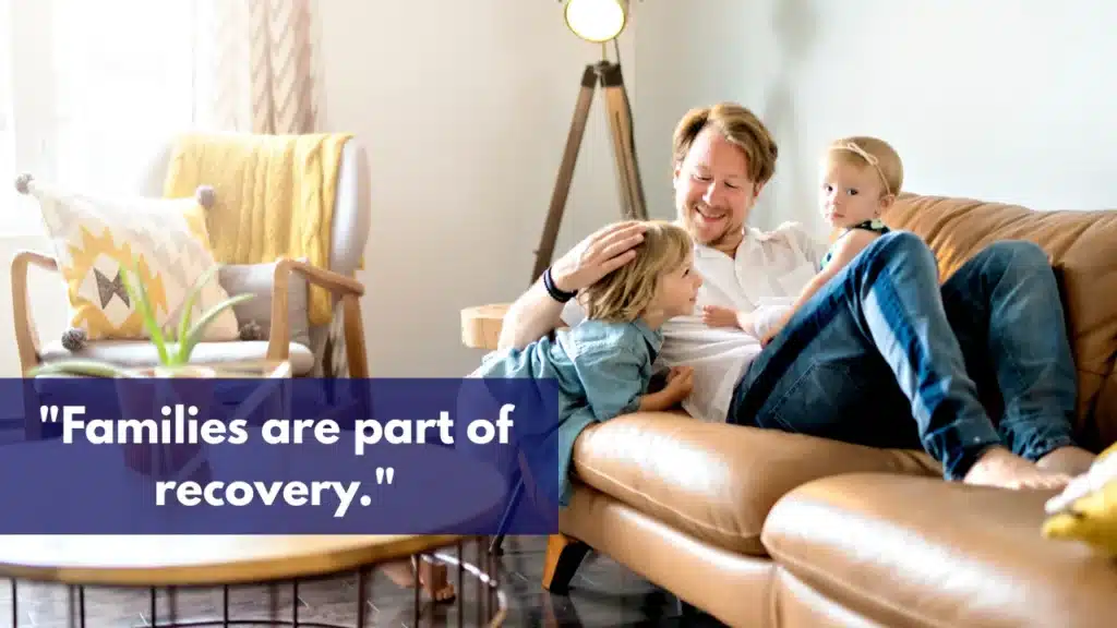 Father sitting on a couch with two young children, smiling together with the quote ‘Families are part of recovery.’ displayed across the image.