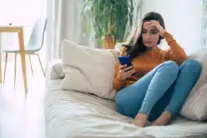 Person sitting on couch using phone looking for heroin addiction treatment.