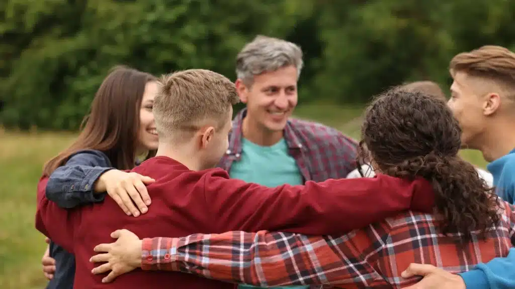 Group of people standing outdoors with arms around each other, symbolizing connection and recovery support.