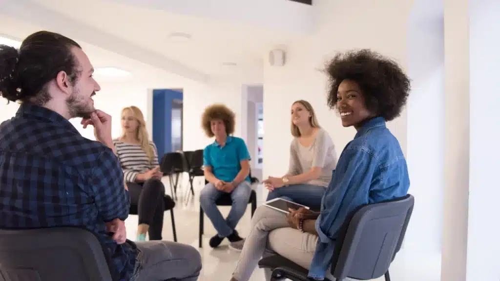People sitting in a therapy circle discussing recovery, symbolizing the benefits of group counseling for addiction treatment.