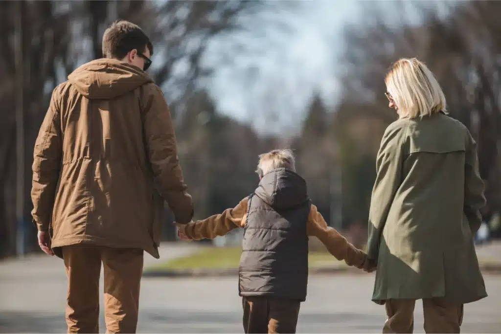Parents holding a child’s hands while walking outdoors in a park.