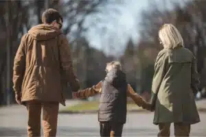Parents holding a child’s hands while walking outdoors in a park.