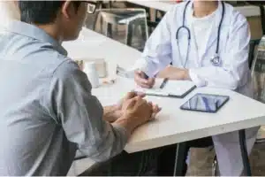 Medical appointment showing a patient and doctor talking across a desk with notes and a tablet