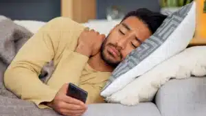 Man lying on a couch looking distressed while holding a phone, representing early alcohol withdrawal symptoms at home