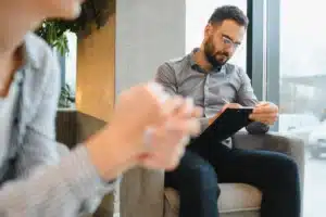 Therapist taking notes on a clipboard during a counseling session with a client in an office setting.