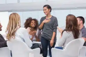 A woman shares during a group therapy session as fellow participants applaud, part of an intensive outpatient program.