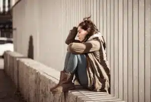 A young woman sitting alone outdoors, looking distressed, reflecting the emotional warning signs of a substance use disorder. A young woman sitting alone outdoors, looking distressed, reflecting the emotional warning signs of a substance use disorder.