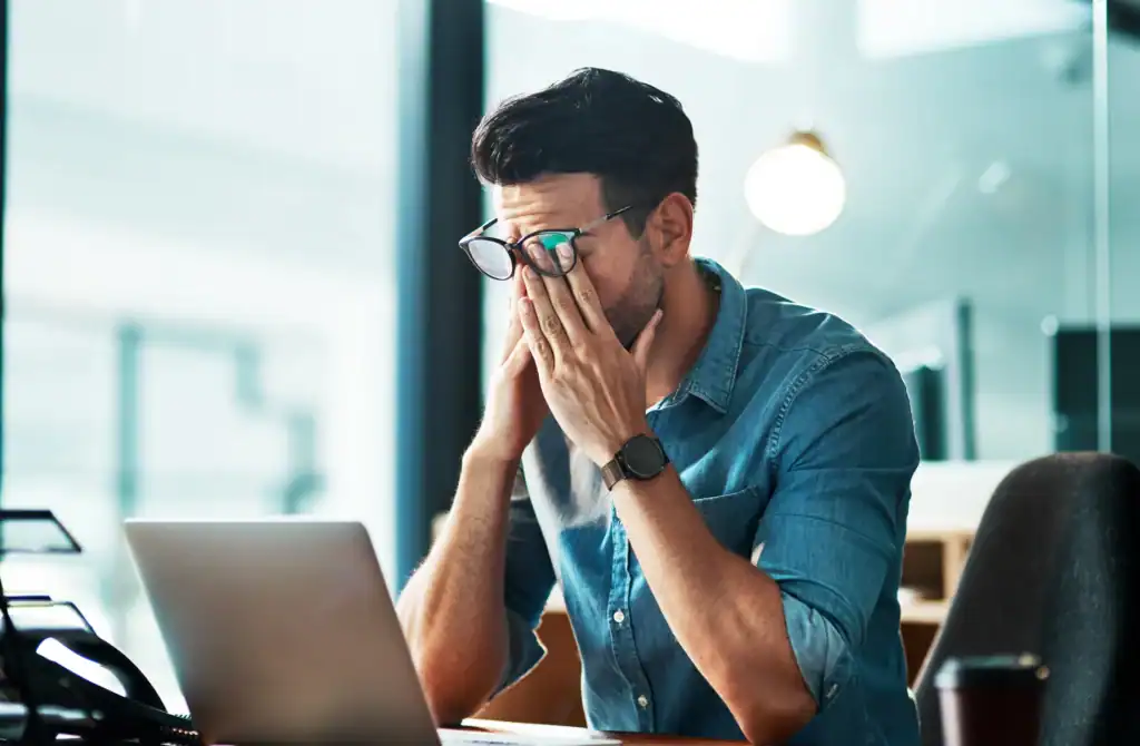 Person at a work desk with their hands to their face, reflecting concerns about job security when entering addiction treatment.